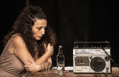 Photo Une femme est assise à table, l'air inquiet avec une bouteille et un verre. Elle écoute la radio.